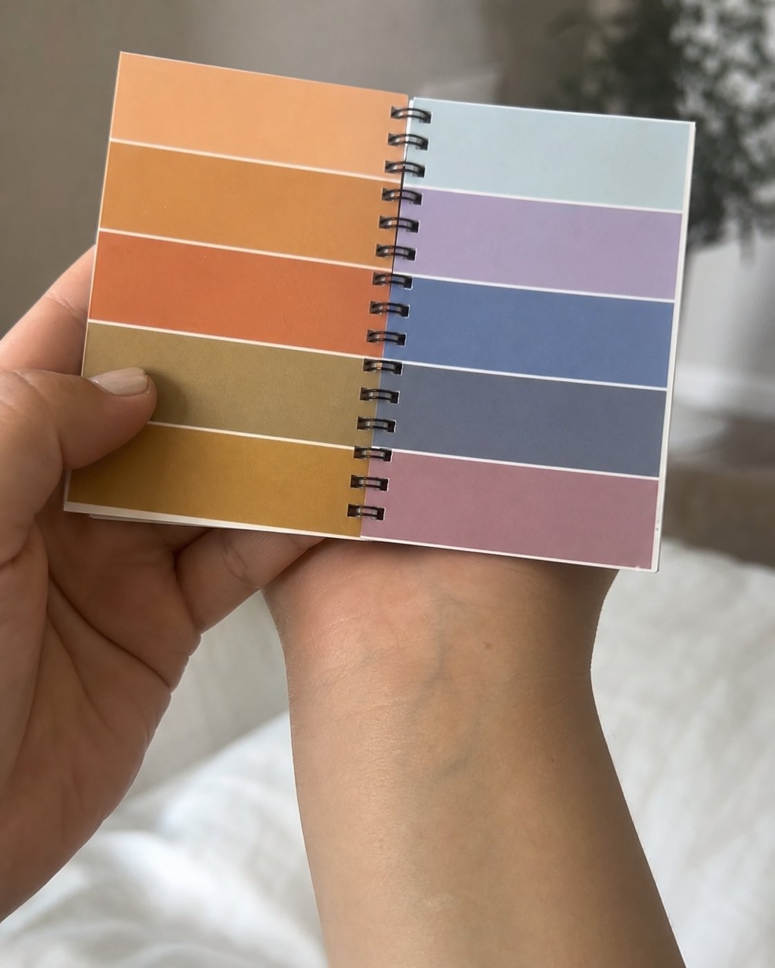 Mano sosteniendo un cuaderno de muestras de color en espiral con franjas de tonos cálidos y fríos